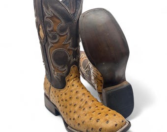 May include: A pair of brown and tan cowboy boots with ostrich skin pattern. The boots have a pointed toe and a decorative stitching design on the shaft.