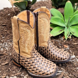 May include: A pair of brown leather children's cowboy boots with a woven pattern. The boots have a zipper on the side and a pointed toe.