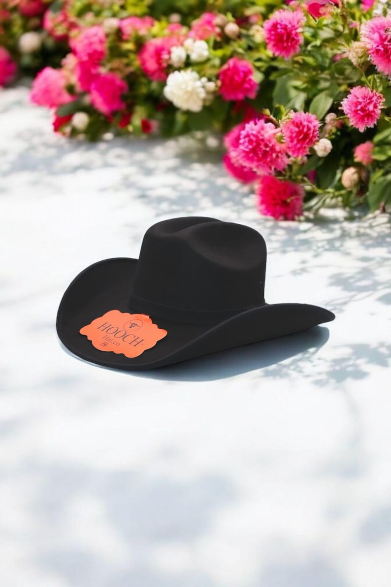 Puede incluir: Un sombrero vaquero de fieltro negro con un ala ancha y una peque&ntilde;a etiqueta naranja que dice "HOOCH" en blanco.