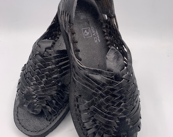 May include: A pair of black leather sandals with a woven design. The sandals have a closed toe and an open heel. The brand name "CLASSIC" is visible on the insole.