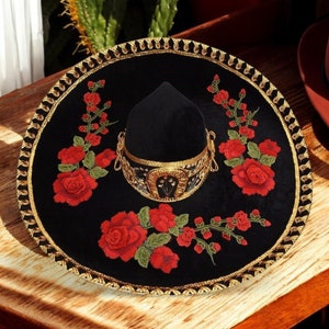 May include: A black sombrero with gold trim and red embroidered roses. The sombrero has a black velvet crown and a wide brim.