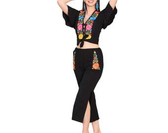 Puede incluir: Conjunto de dos piezas negro con bordados florales coloridos. La parte superior tiene cuello en V y cierre de lazo, mientras que los pantalones tienen aberturas laterales. El conjunto es elegante.
