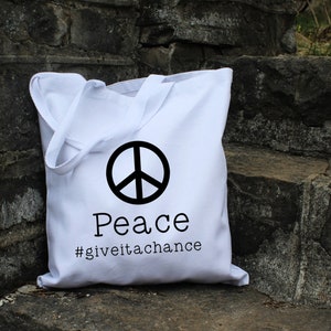 May include: White canvas tote bag with a black peace sign and the text "Peace #giveitachance".