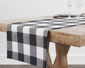 Puede incluir: Un camino de mesa a cuadros en blanco y negro sobre una mesa de madera. El camino de mesa está hecho de un tejido suave y tejido con un brillo sutil.