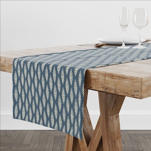 May include: A blue table runner with a white leaf pattern. The runner is on a wooden table with two wine glasses and a plate.