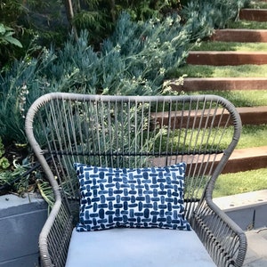 May include: A wicker chair with a blue and white patterned cushion. The chair is outdoors on a patio with a green lawn and wooden steps in the background.