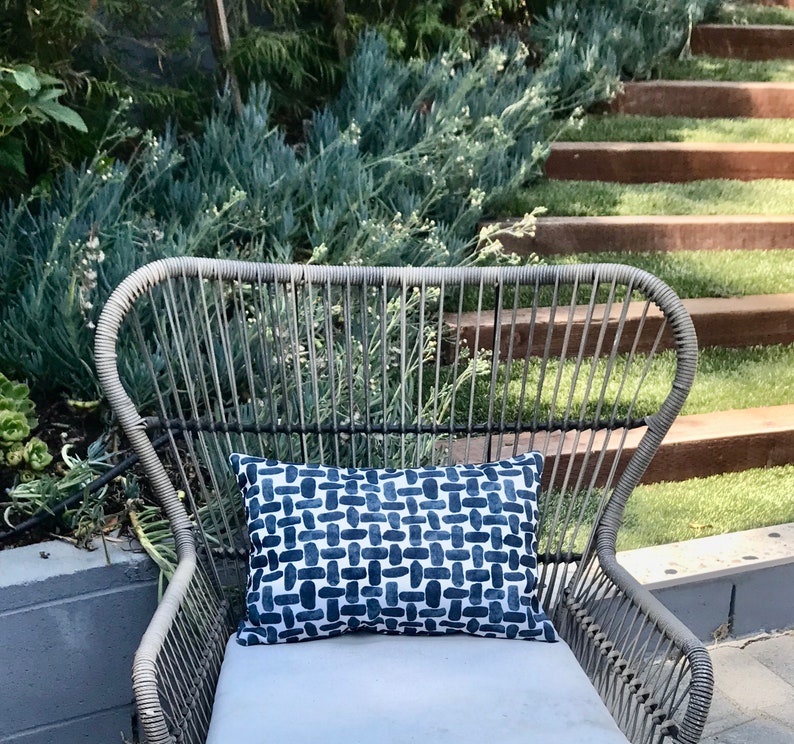 May include: A wicker chair with a blue and white patterned cushion. The chair is outdoors on a patio with a green lawn and wooden steps in the background.
