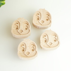 Könnte beinhalten: Vier Holzspielblöcke mit einem geschnitzten Comic-Gesicht auf jedem. Die Blöcke sind hellbraun und haben ein einfaches Design.