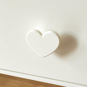 Könnte beinhalten: Weiße Kommodenschublade mit einem herzförmigen weißen Knopf.