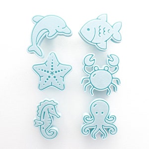 Op de afbeelding: Set van zes blauwe schuimstempels met verschillende zeedieren, waaronder een dolfijn, een vis, een zeester, een krab, een octopus en een zeepaardje.