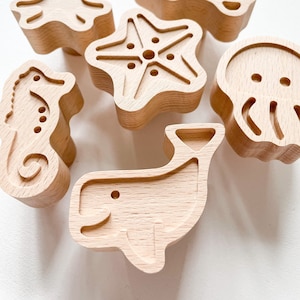 Op de afbeelding: Set van zes houten zeedieren speelgoed, waaronder een octopus, schildpad, zeester, kwal, walvis en zeepaardje. Het speelgoed is allemaal in natuurlijke houtkleur en heeft een gladde afwerking.