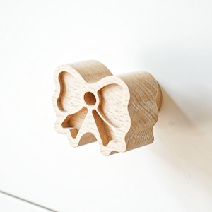 May include: A wooden drawer pull shaped like a bow. The bow is carved from light wood and has a simple design.