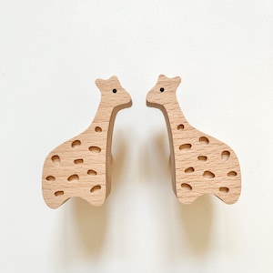 Könnte beinhalten: Zwei Wandhaken aus Holz in Giraffenform mit hellbrauner Oberfläche und gepunktetem Muster.