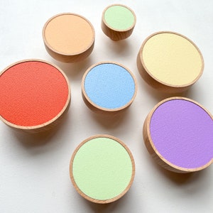 Peut inclure: Six boutons ronds en bois avec des dessus de couleurs différentes. Les boutons sont dans différentes nuances d'orange, jaune, vert, bleu et violet.