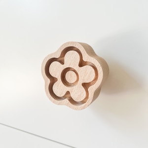 Könnte beinhalten: Ein hölzerner Schubladenknauf in Form einer Blume mit einem einfachen Design. Der Knauf ist hellbraun und hat eine glatte Oberfläche.