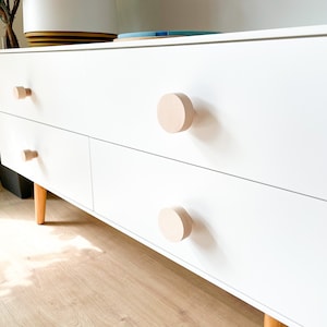 Könnte beinhalten: Eine weiße Kommode mit vier Schubladen und Holzgriffen. Die Kommode hat ein modernes Design und ist aus Holz. Die Kommode steht auf einem Holzboden.