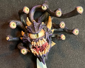 May include: A purple and black painted miniature of a beholder with multiple eyes, a large mouth with sharp teeth, and a treasure chest on a black base.