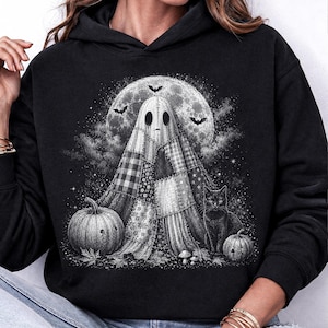 May include: A black hooded sweatshirt featuring a graphic print of a patchwork ghost standing in front of a large full moon. The design includes a black cat, two pumpkins, and small bats flying in the night sky, rendered in shades of white and gray.
