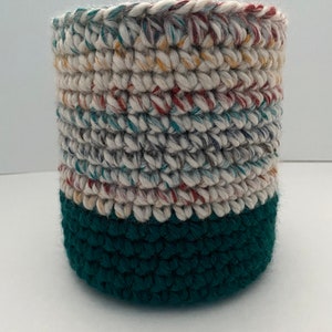 May include: A crocheted basket with a white and multi-colored top and a solid green bottom.