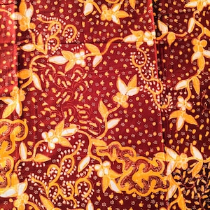May include: Red fabric with a repeating pattern of white and yellow floral designs. The fabric has a small-scale, intricate pattern.