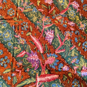 May include: A close-up of a colorful fabric with a repeating pattern of flowers and leaves. The fabric is a mix of green, red, orange, yellow, and blue.