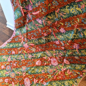 May include: A colorful fabric with a repeating pattern of flowers and leaves. The fabric is a mix of orange, green, pink, and yellow.