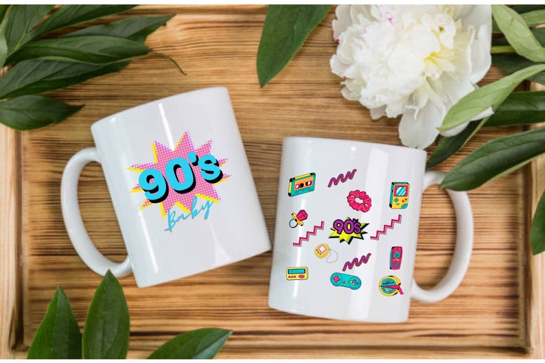 May include: Two white ceramic mugs with 90's themed designs. One mug features a pink and blue graphic with the text "90's Baby". The other mug has a white background with a variety of 90's themed graphics, including a cassette tape, a scrunchie, a game console, and a pacifier.