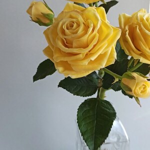 May include: A bouquet of yellow roses in a clear glass vase with a textured surface. The roses are arranged in a simple, elegant style.