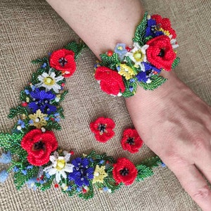May include: A beaded flower necklace and bracelet set with red, blue, white, and yellow flowers. The set is made of small beads and is a delicate and intricate piece of jewelry.