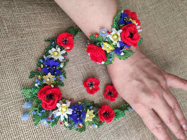 May include: A beaded flower necklace and bracelet set with red, blue, white, and yellow flowers. The set is made of small beads and is a delicate and intricate piece of jewelry.