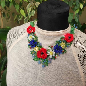 May include: A beaded necklace with a floral design. The necklace features red, blue, white, and yellow flowers with green leaves. The necklace is on a black mannequin.