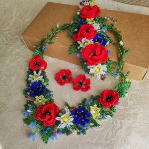 May include: A beaded flower necklace and earrings set with red poppies, white daisies, blue forget-me-nots, and green leaves.