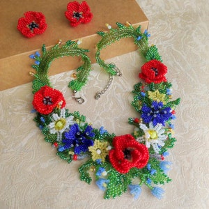 May include: A beaded necklace with a floral design featuring red poppies, blue and white flowers, and green leaves. The necklace is accompanied by a pair of matching earrings.