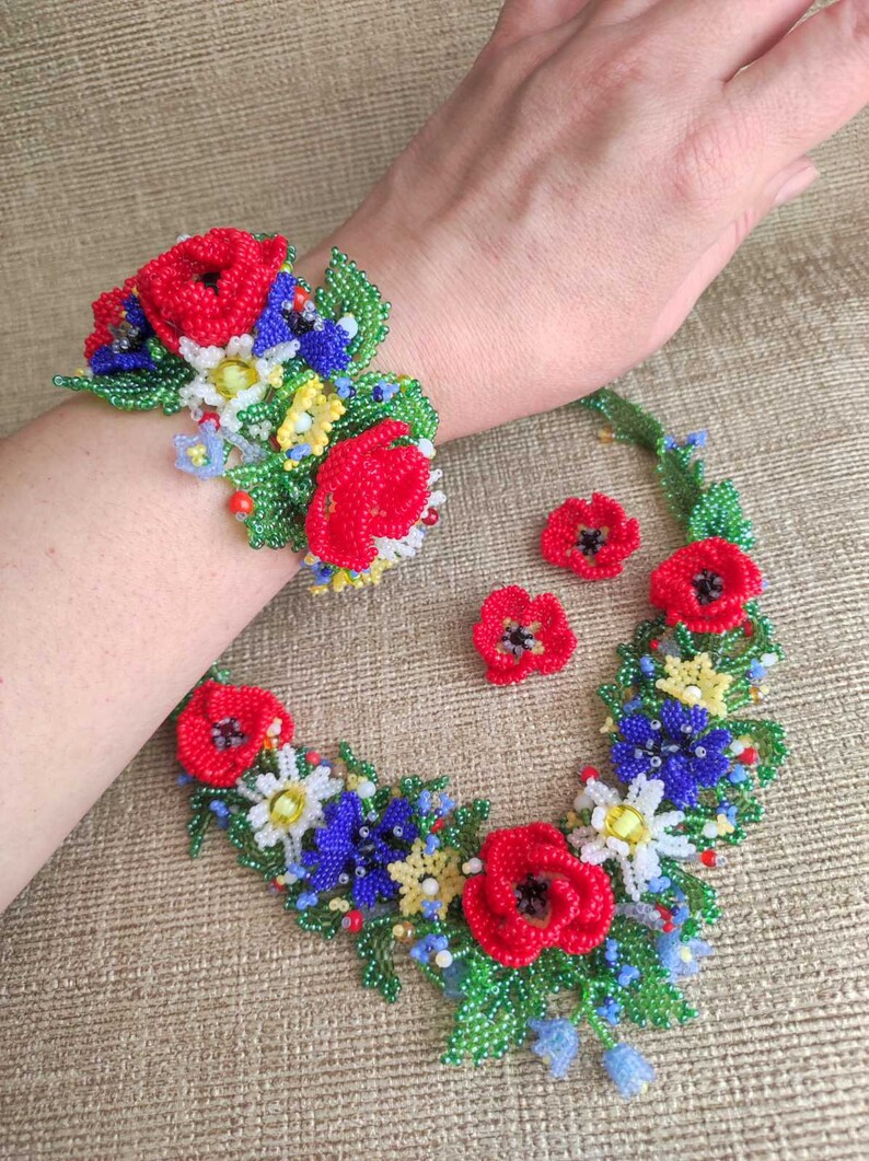 May include: A beaded flower necklace and bracelet set with red, blue, green, and yellow flowers. The set also includes a pair of matching earrings.