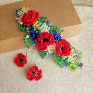 May include: A beaded bracelet and earrings set featuring red poppy flowers with green leaves and white, yellow, and blue accents.