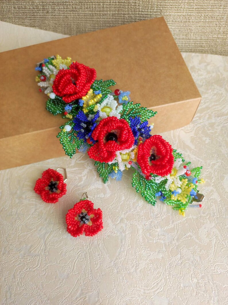 May include: A beaded bracelet and earrings set featuring red poppy flowers with green leaves and white, yellow, and blue accents.