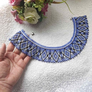 May include: A blue and white beaded necklace with a geometric pattern. The necklace is made of small beads and has a scalloped edge.