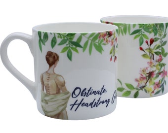 May include: White ceramic mug featuring a floral design and a woman in a white robe. The text "Obstinate, Headstrong & Graceful" is printed on the mug.