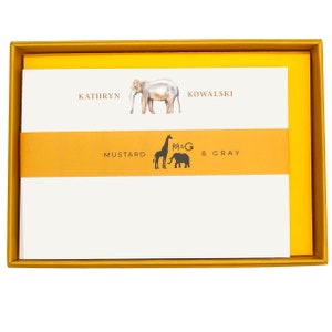May include: A box of stationery with a yellow background and a white elephant illustration. The text on the box reads "Kathryn Kowalski Mustard & Gray".