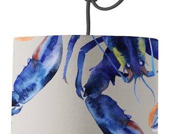 May include: A gray lampshade with a watercolor pattern of blue lobsters. The lampshade is cylindrical and has a black cord.