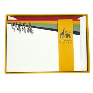 May include: A box of yellow and red stationery cards with a white envelope. The cards feature a black and white illustration of cyclists racing and a rainbow stripe design. The box has a yellow label with the text "M&G Mustard & Gray".