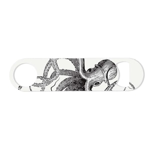 May include: A white bottle opener featuring a detailed black and white illustration of an octopus. The octopus design is centered on the opener, with a circular opening on one end and a bottle cap opener on the other.