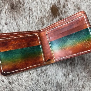 May include: A brown leather wallet with a green and orange ombre design. The wallet has multiple card slots and a billfold. The wallet is open and the inside is visible.