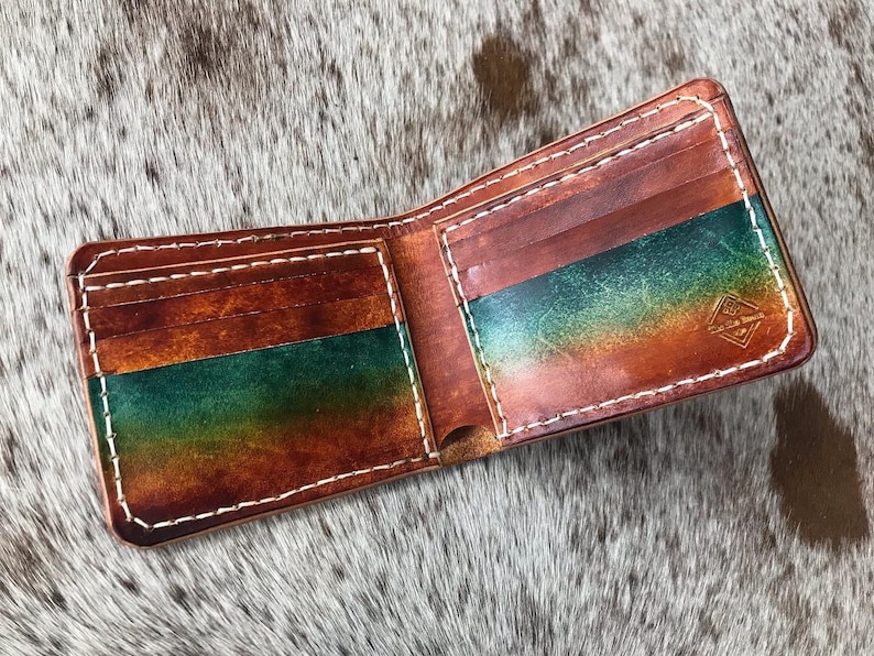 May include: A brown leather wallet with a green and orange ombre design. The wallet has multiple card slots and a billfold. The wallet is open and the inside is visible.