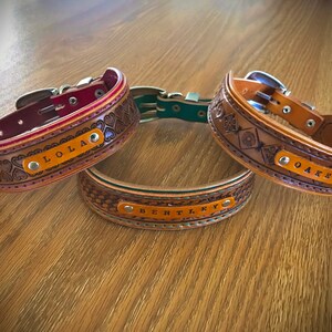 Puede incluir: Tres collares de perro de cuero con diferentes dise&ntilde;os y nombres personalizados: Lola, Bentley y Oakley. Los collares son marrones con un ribete rojo, verde y marr&oacute;n.