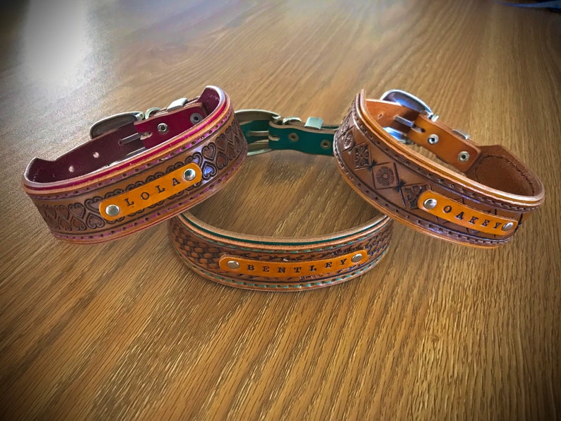Puede incluir: Tres collares de perro de cuero con diferentes dise&ntilde;os y nombres personalizados: Lola, Bentley y Oakley. Los collares son marrones con un ribete rojo, verde y marr&oacute;n.