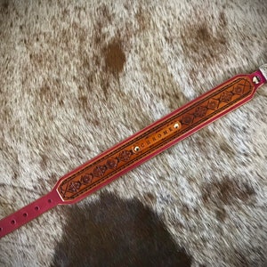 Puede incluir: Un collar de perro de cuero rojo con una hebilla plateada y dise&ntilde;os en relieve intrincados. El collar est&aacute; personalizado con el nombre "CHROME".
