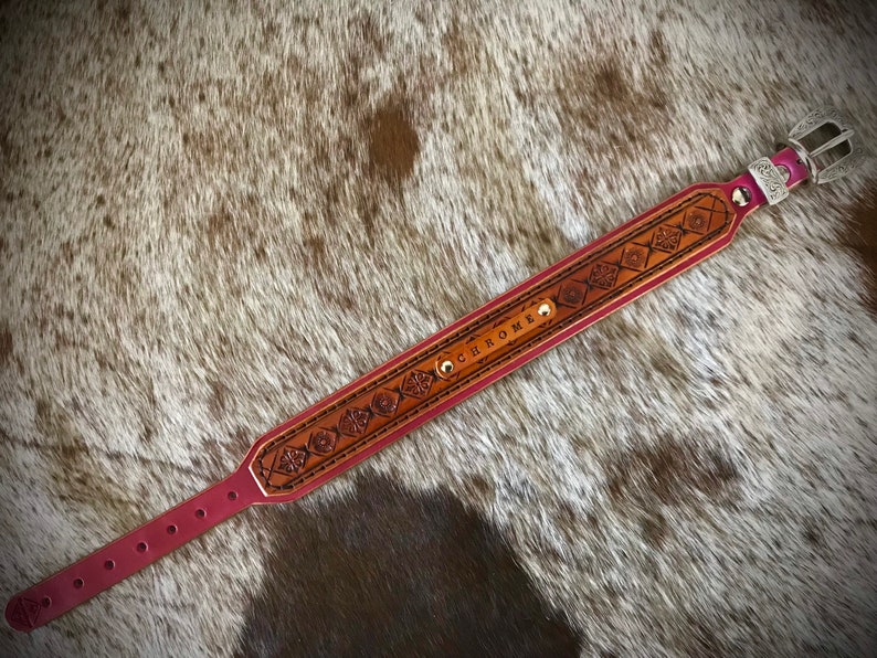 Puede incluir: Un collar de perro de cuero rojo con una hebilla plateada y dise&ntilde;os en relieve intrincados. El collar est&aacute; personalizado con el nombre "CHROME".