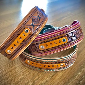 Puede incluir: Tres collares de perro de cuero con nombres personalizados: "Oakey", "Lola" y "Bentley". Los collares son marrones con diferentes dise&ntilde;os en relieve y costuras.