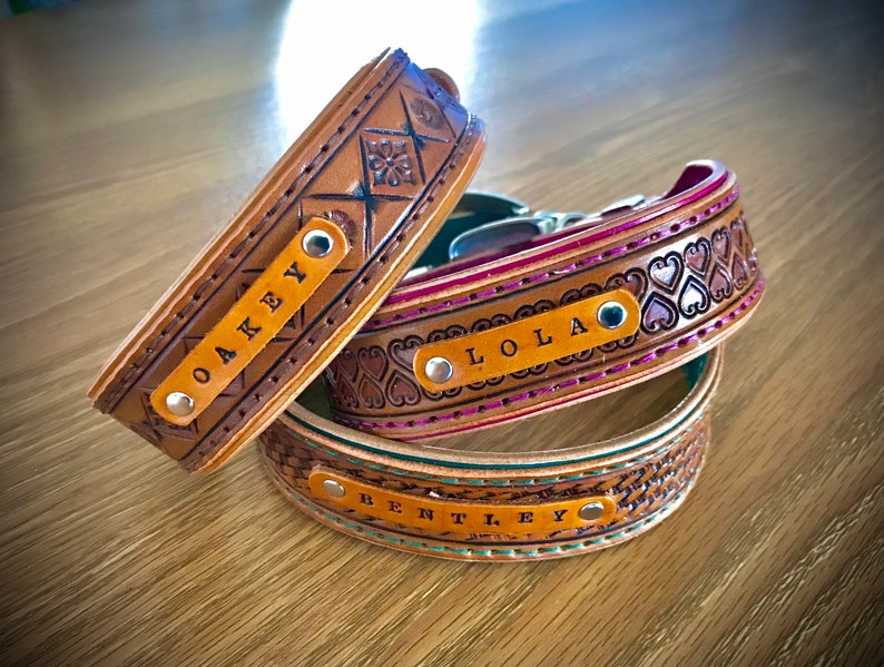 Puede incluir: Tres collares de perro de cuero con nombres personalizados: "Oakey", "Lola" y "Bentley". Los collares son marrones con diferentes dise&ntilde;os en relieve y costuras.